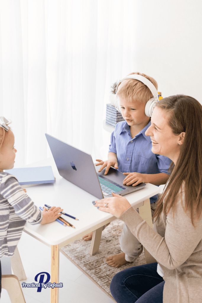 Mom with two small children, one has headphones and a computer. One is playing with colored pencils